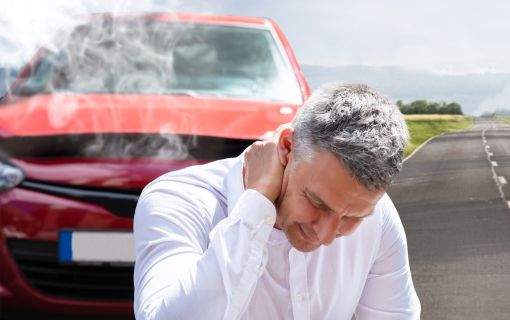 煙が上がる車の前で落ち込む男性